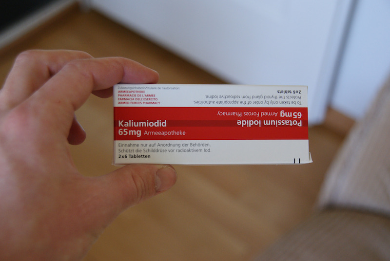 Hand holding a Swiss Armeeapotheke box of potassium iodide tablets.