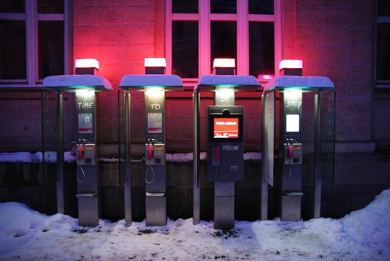 Four public telephone kiosks standing in snow beneath a red-lit building.