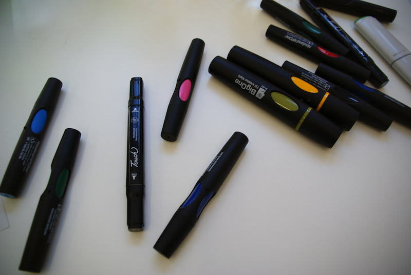 Black permanent markers with colored caps scattered on a white surface.