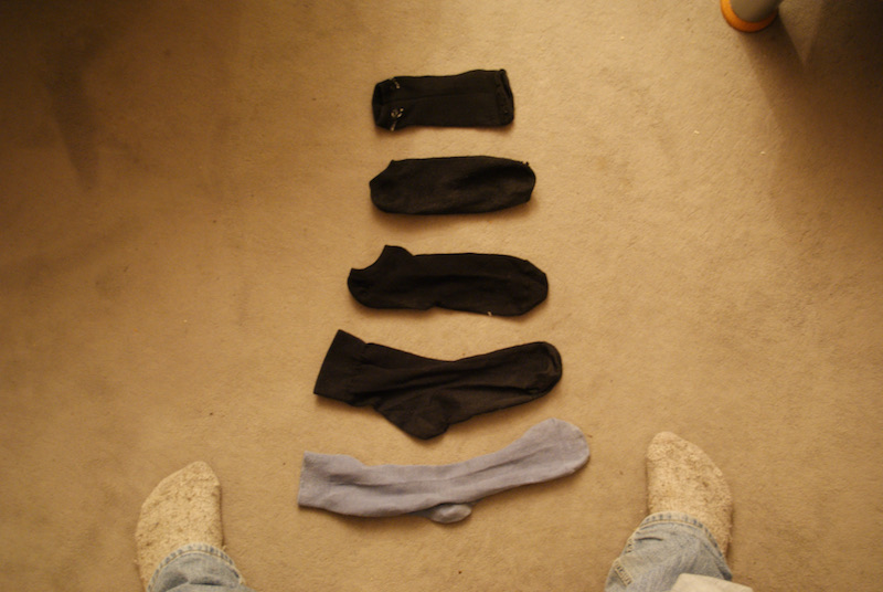 Five socks arranged on a beige carpet between a person’s feet.