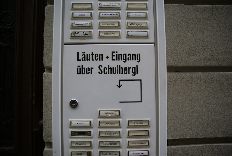 Apartment-building intercom with nameplates and a German direction sign.