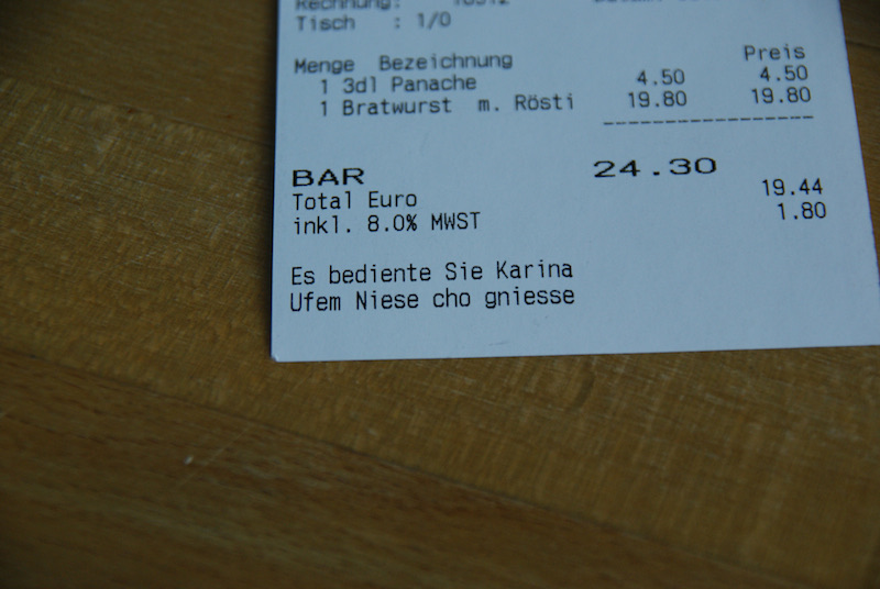Restaurant receipt on a wooden table showing an itemized bill and a personalized service message.