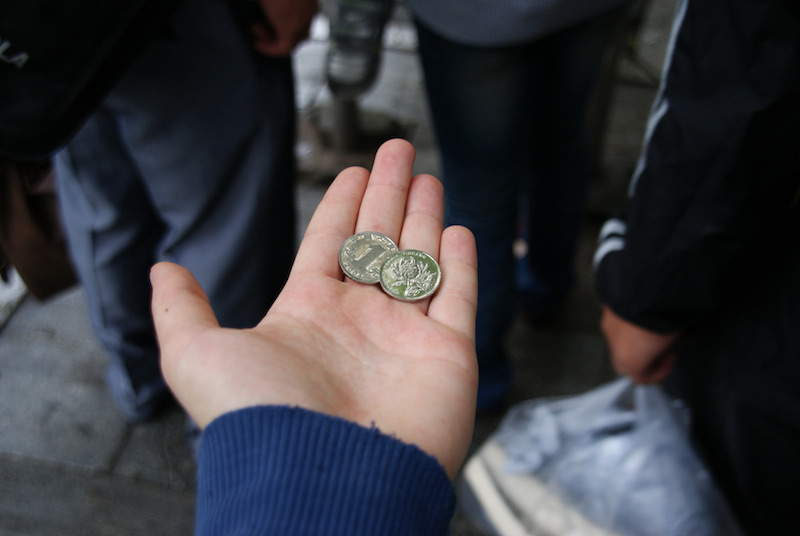 Open hand holding two Chinese coins among people standing on a pavement.