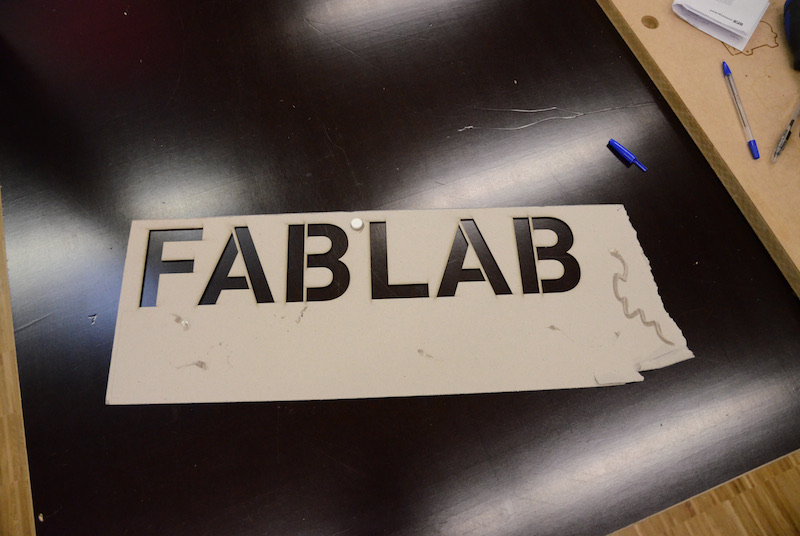 Laser-cut sign reading ‘FABLAB’ on a worktable.