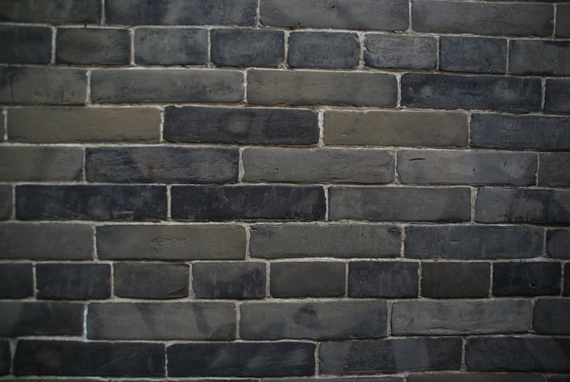 Close view of a dark gray brick wall with irregularly colored bricks.