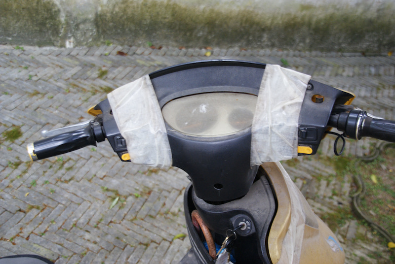 Top view of a scooter handlebar and dashboard wrapped in white duct tape.