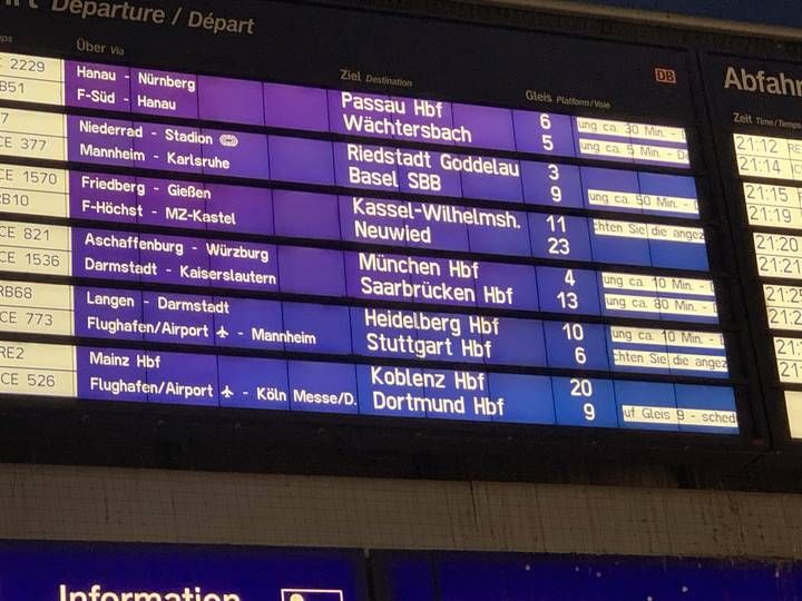 A blue departure board at a German train station shows destinations, platform numbers and multiple delay messages.