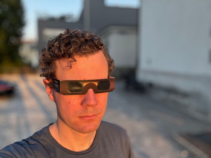 A person wearing black cardboard eclipse glasses in the warm, dim light of a solar eclipse.