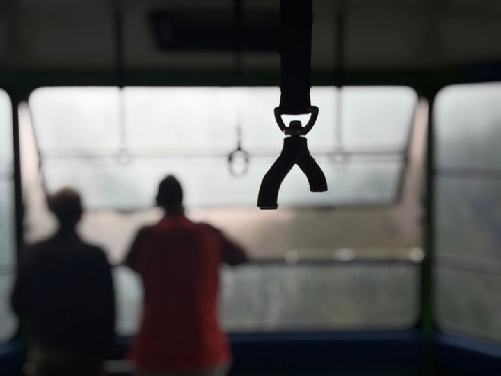 A broken black handgrip hangs in sharp focus, with two blurred people and bright windows behind it.