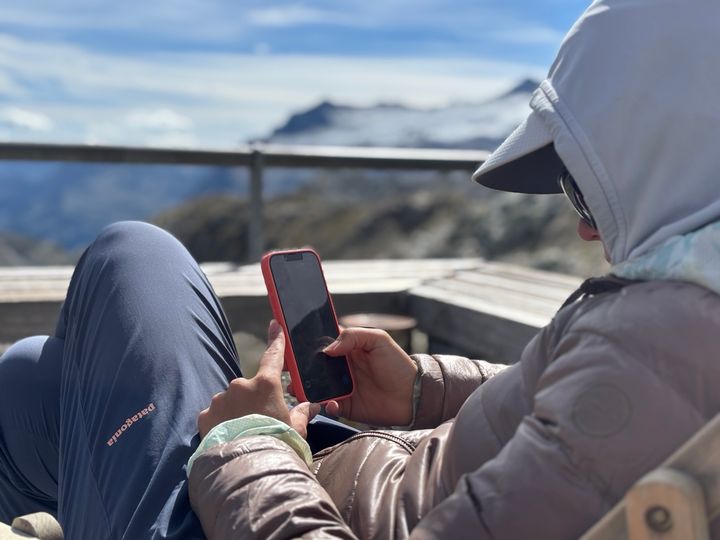 A seated person looking at a smartphone with a mountain landscape in the background.