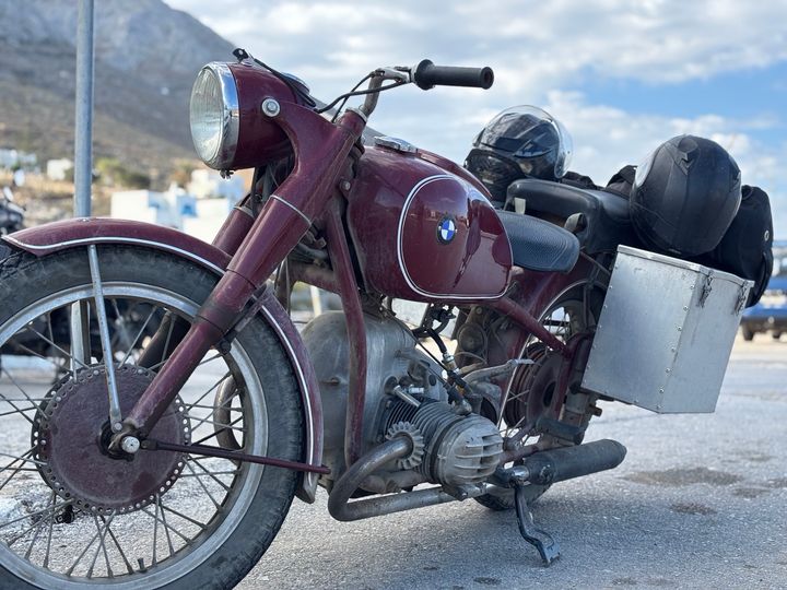 A burgundy BMW motorcycle with an aluminum luggage box and two helmets.